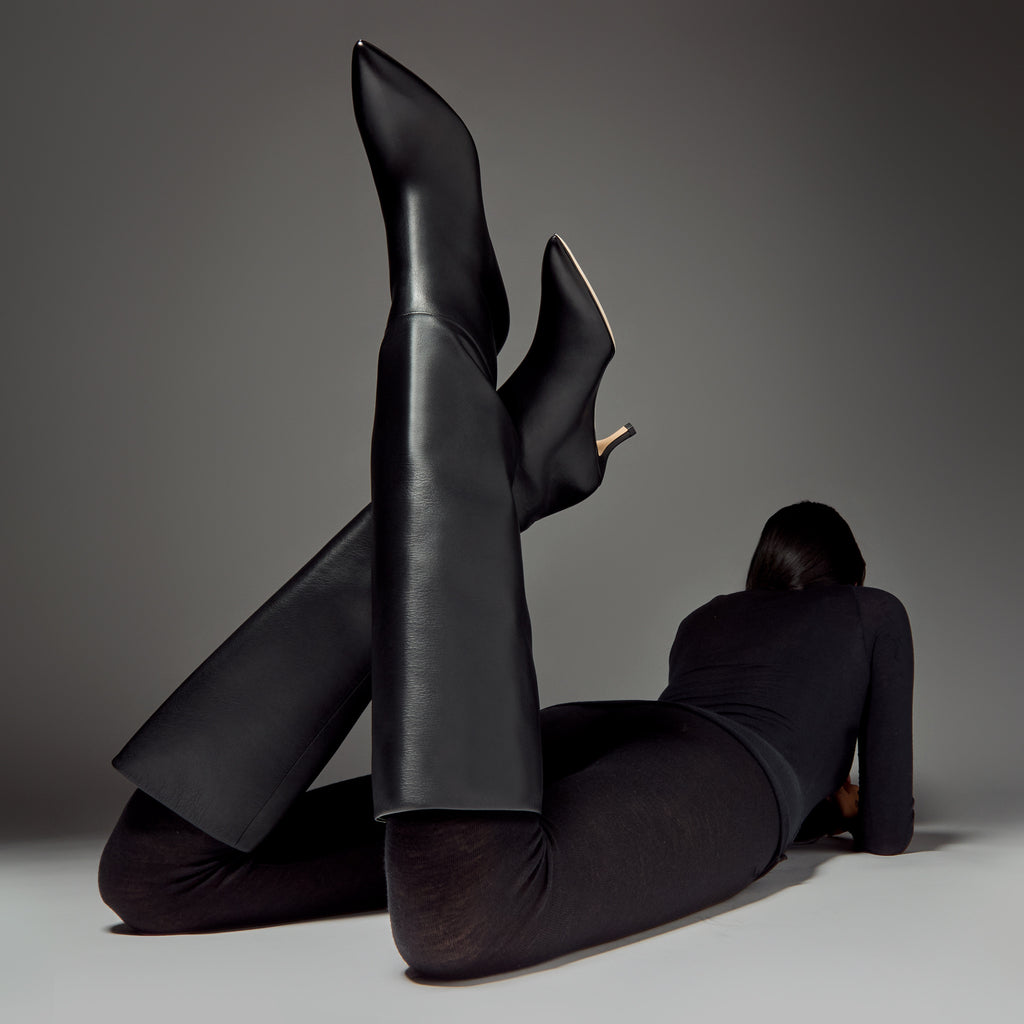 black leather slouchy knee boots on model with black outfit in minimal studio setting