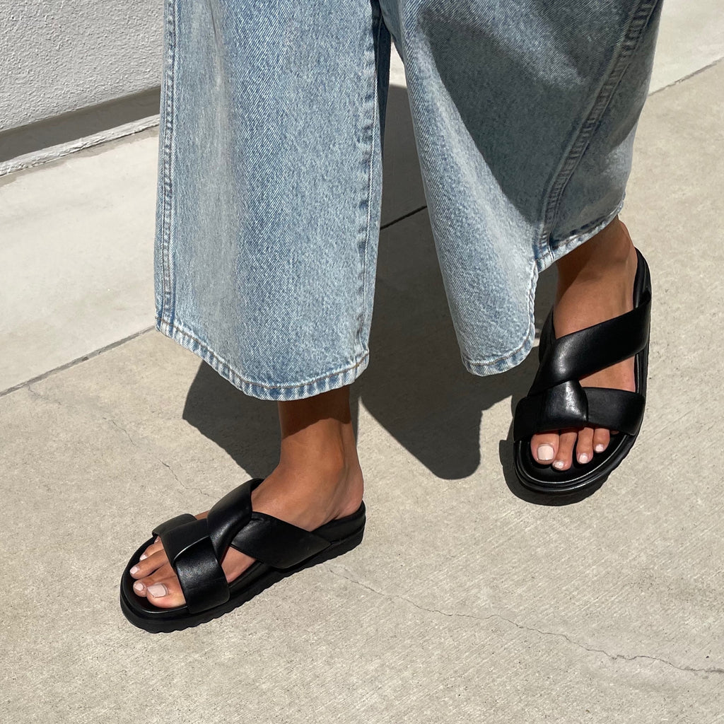 Neil J Rodgers black Obi two sandal with a two-strap style made from padded leather straps, with comfortable flat footbed and lightweight thick black sole paired with light wash wide-leg denim.