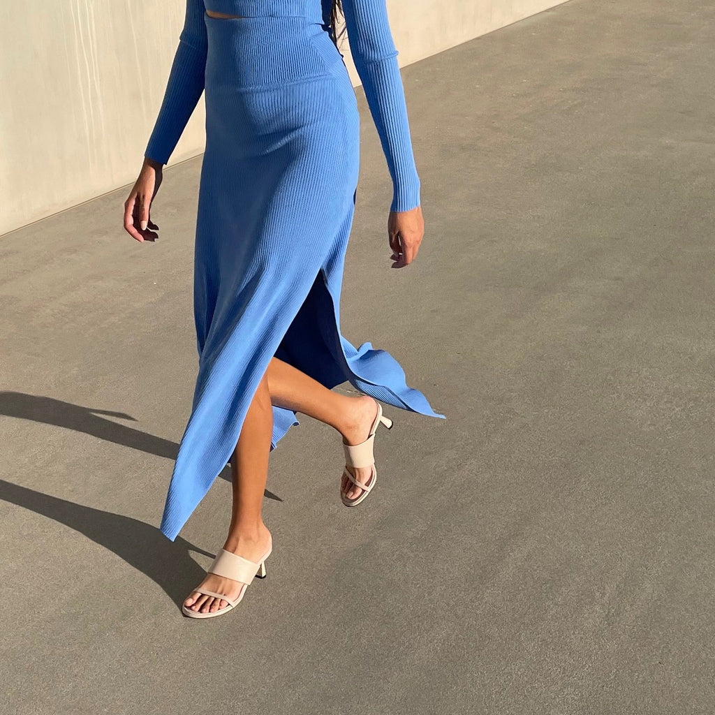 Neil J Rodgers off white Alma sandal has a rounded toe, stretch nappa leather instep strap, thin toe strap, padded footbed, and comfortable 60mm heel and is styled with a blue long sleeve and midi skirt set.
