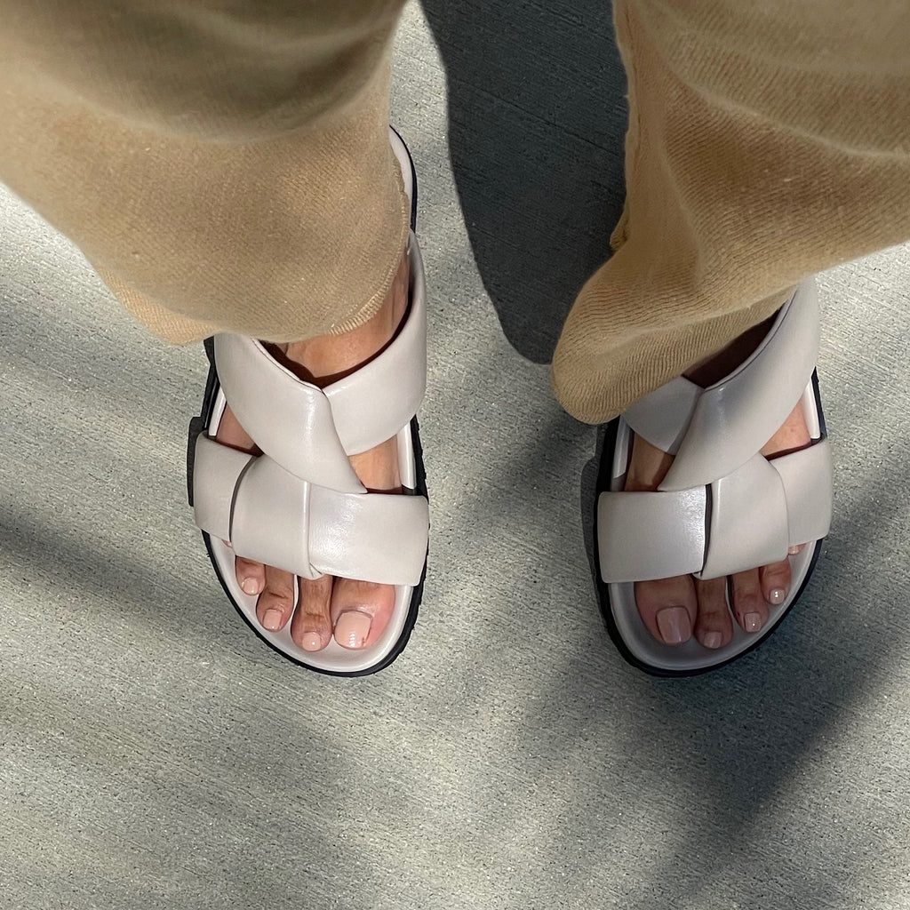 Neil J Rodgers off-white Obi two sandal with a two-strap style made with padded leather straps, a comfortable flat footbed and lightweight thick black sole paired with camel knit pants.