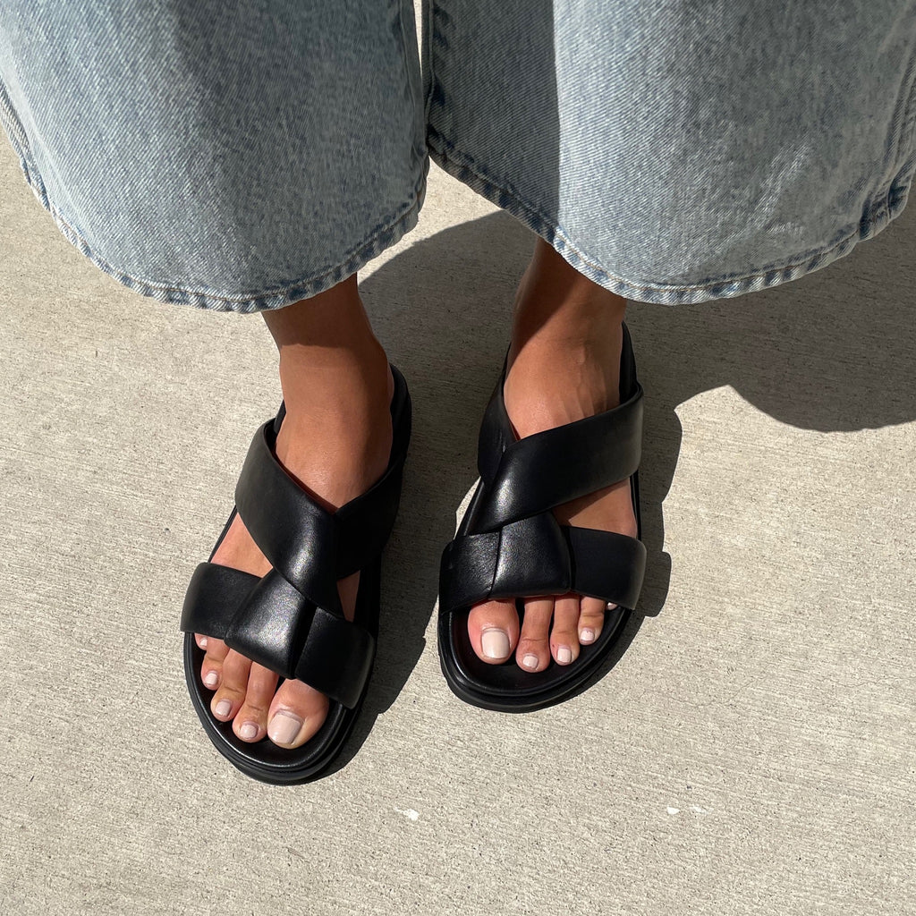 Neil J Rodgers black Obi two sandal with a two-strap style made from padded leather straps, with comfortable flat footbed and lightweight thick black sole paired with light wash wide-leg denim.
