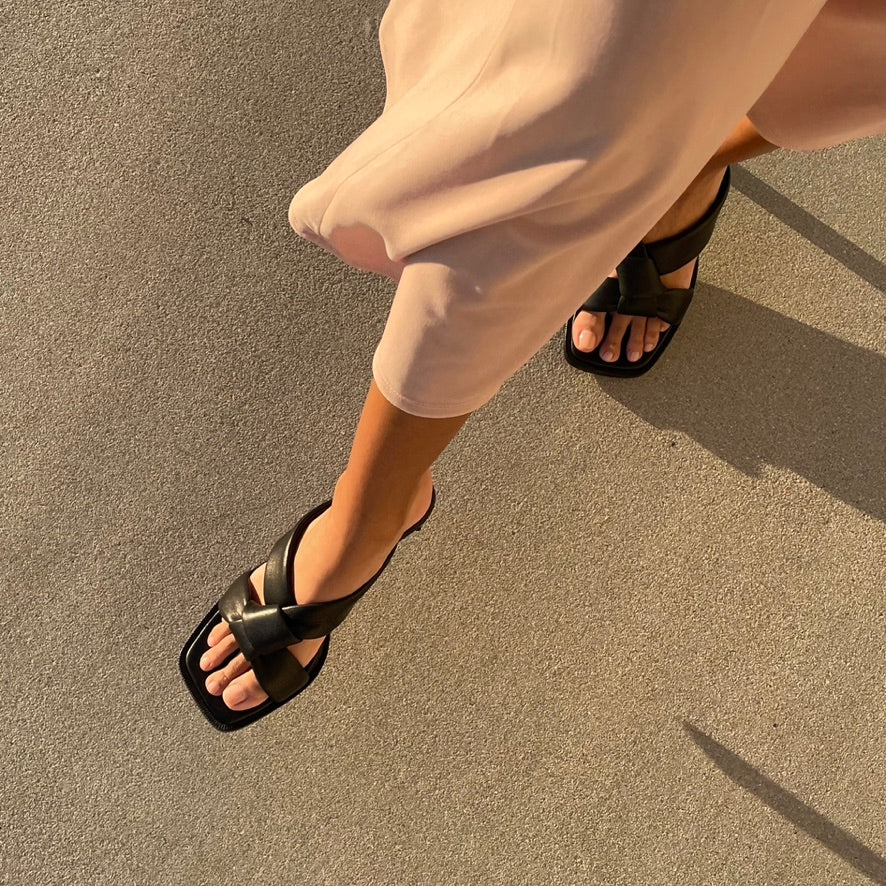 Neil J Rodgers Obi heel with signature padded leather, knotted obi strap sandal with an exaggerated square toe and modern heel in black nappa leather worn with a midi length dress.