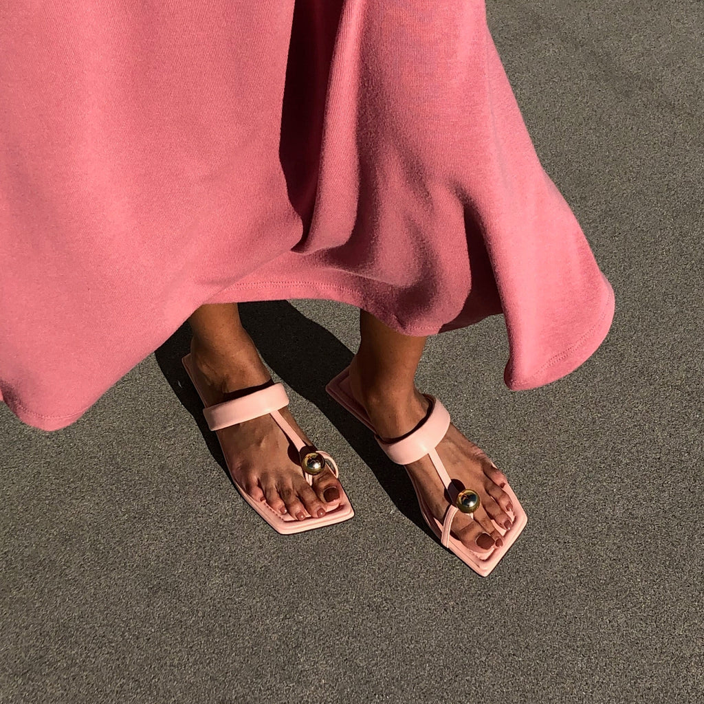 Neil J Rodgers pink Samira sandal with a flat footbed, minimal leather straps and gold bead embellishment paired with a pink midi dress.