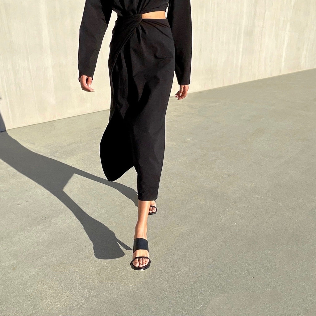 Neil J Rodgers black Alma sandal has a rounded toe, stretch nappa leather instep strap, thin toe strap, padded footbed, and comfortable 60mm heel and is styled with black long sleeve midi dress.