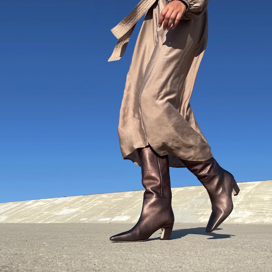 Neil J Rodgers Meg knee high boots with a pointed square toe made from soft, bronze metallic Italian nappa leather paired with a gold midi dress.