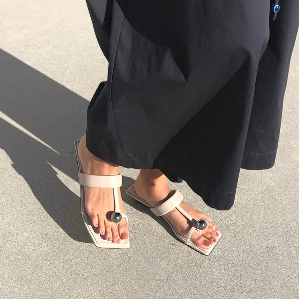 Neil J Rodgers off-white Samira sandal with a flat footbed, minimal leather straps and silver bead embellishment paired with wide leg, lightweight black pants.
