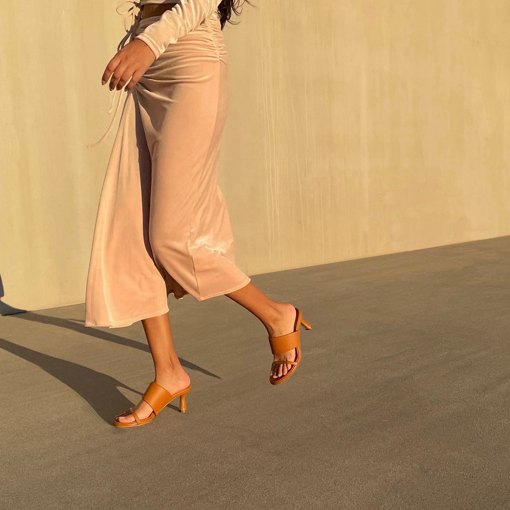 Neil J Rodgers cognac Alma sandal has a rounded toe, stretch nappa leather instep strap, thin toe strap, padded footbed, and comfortable 60mm heel and is styled with blush velvet long sleeve midi dress.