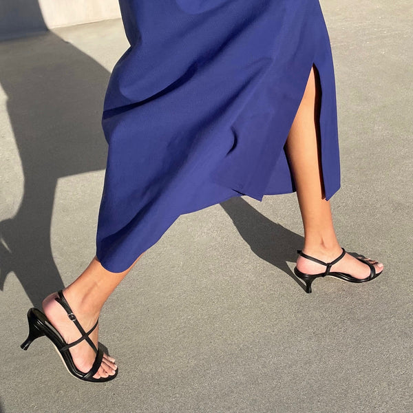 Neil J Rodgers Haze sandal with a round toe, minimal styling, and comfortable 55mm heel in soft black Italian nappa leather is paired with a deep blue midi length dress.
