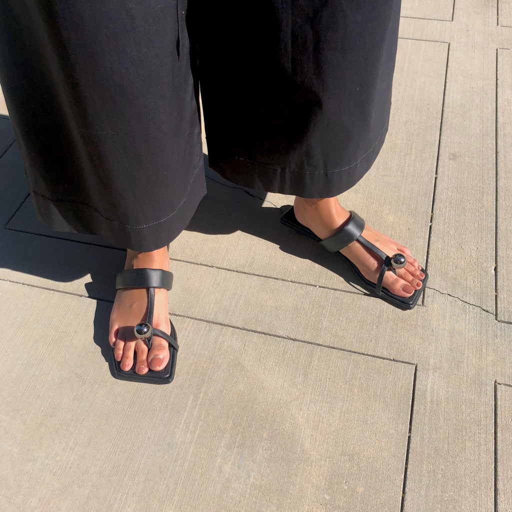Neil J Rodgers black Samira sandal with a flat footbed, minimal leather straps and silver bead embellishment paired with wide leg, lightweight black pants.