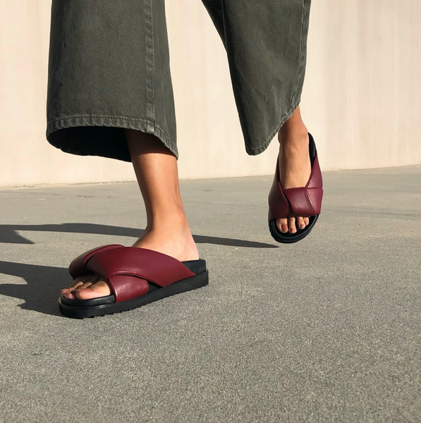 Neil J Rodgers burgundy Obi slide sandal with padded leather straps, comfortable flat footbed and lightweight thick black sole paired with black wide leg denim pants.